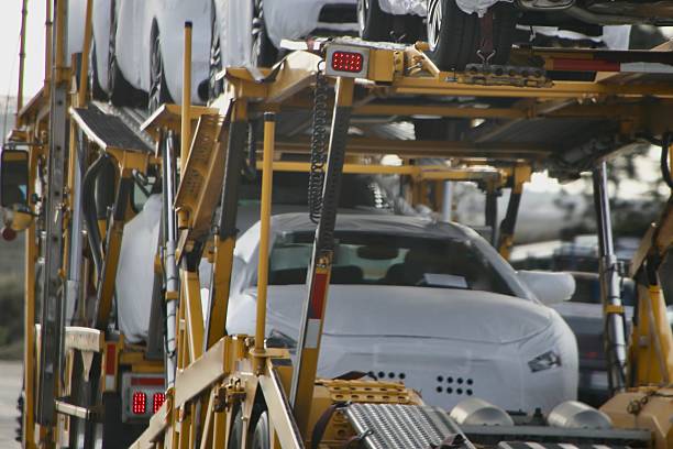 Several new white cars, covered in protective wrap, are stacked on a yellow car carrier truck, ready for transport. The photo is taken from the rear, showing the vehicles and trailer structure—an impressive display of professional Car Transport Orangevale, CA services in action.